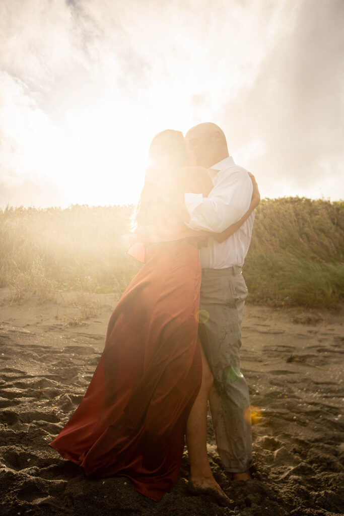 Couple hugging with golden sunflare during romantic engagement session at Blowing Rocks Preserve beach in Florida.