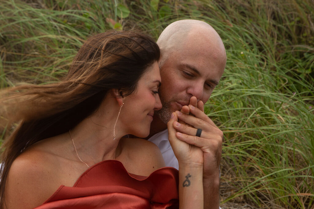 Close-up of man kissing woman’s engagement ring finger during intimate engagement session at Blowing Rocks Preserve, Florida.