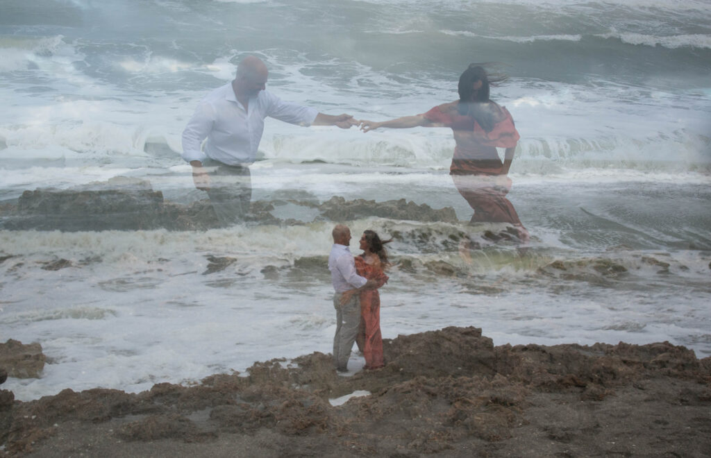 In-camera overlay photo of couple holding hands and embracing on rocky shoreline during artistic engagement session at Blowing Rocks Preserve, Florida.
