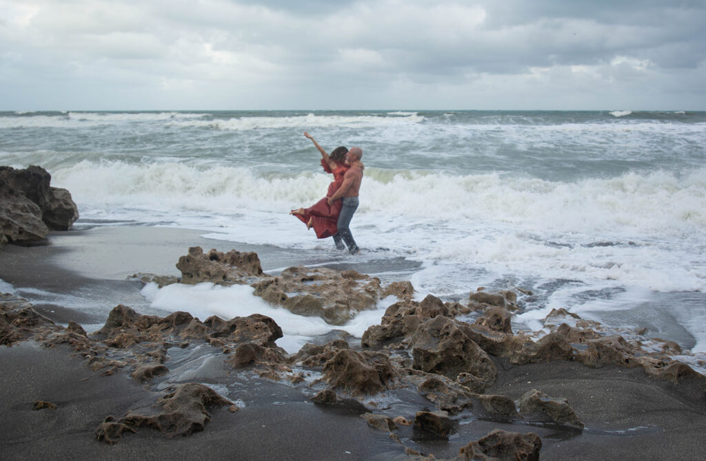 Man lifting woman with arms outstretched in ocean water during joyful engagement session at Blowing Rocks Preserve, Florida.