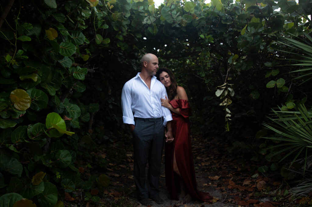 Couple in mangroves with woman leaning on man’s shoulder during intimate engagement session at Blowing Rocks Preserve Florida.