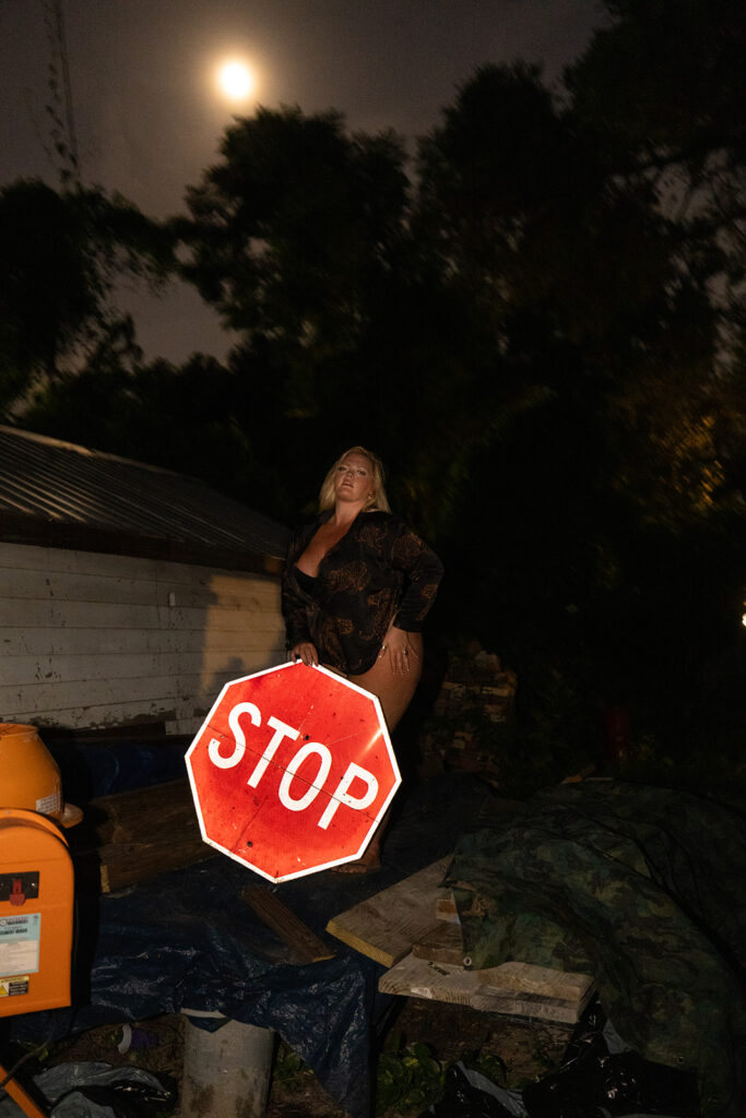 Blonde woman posing with one hand on her butt while holding a stop sign, blending playful attitude with bold sensuality in a striking boudoir photo.