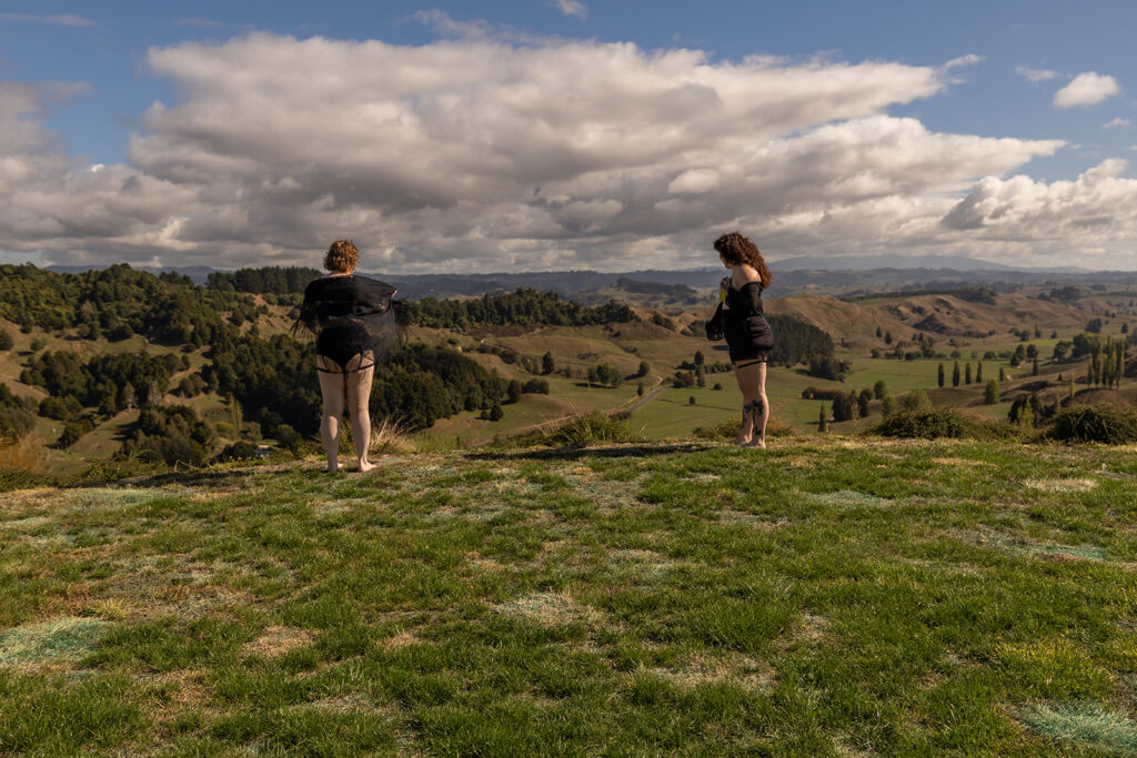 Cecelia and her best friend stand side by side on a wooden deck in Te Kuiti, New Zealand, gazing out at the mountain landscape and soaking in the peaceful view.