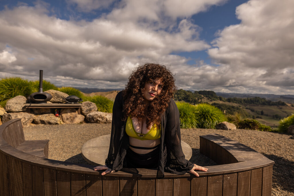 Cecelia leans on a wooden bench in Te Kuiti, New Zealand, gazing confidently at the camera, capturing a moment of elegant, self-assured energy during her boudoir shoot.