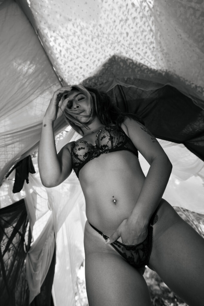 Black-and-white boudoir portrait of a woman in lingerie standing beneath a garden archway, captured from a low angle with strong contrast and elegant composition.