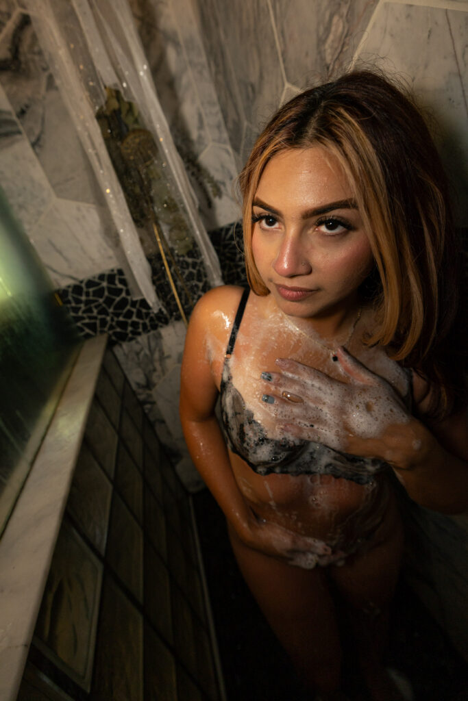 Luxury boudoir portrait of a woman in lingerie standing in a shower, captured with soft lighting, water, and an intimate editorial aesthetic.